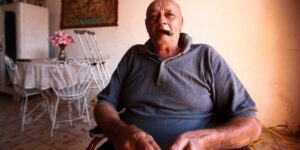 An older adult sitting comfortably in a chair preparing for pelvic tilt exercises in a bright room.
