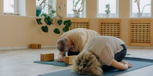An active senior couple performing seated side-bend stretches in a bright, comfortable living room.