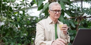 An older adult observing a plant leaf closely with a magnifying glass in a bright garden.