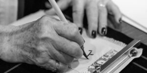 An elderly person practicing calligraphy at a wooden desk with soft lighting.