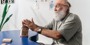 A senior adult performing a seated neck isometric exercise in a sunny living room.