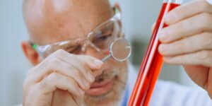 An older adult examining a crystal with a magnifying glass.