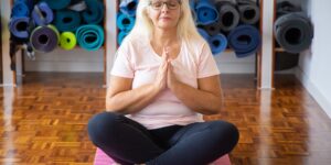 An older adult performing gentle hand stretches while seated in a bright, comfortable room.