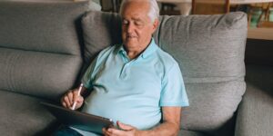 A senior adult using a tablet to navigate digital services in a well-lit modern home.
