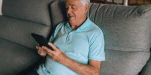 A senior adult using a tablet in a modern, comfortable home office setting.