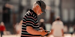 A senior traveler using a smartphone to communicate with a market vendor in a bustling outdoor market.