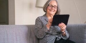 An older adult engaged in digital sketching on a tablet in a sunlit room.